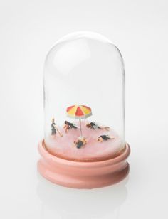 a glass dome with an umbrella inside on top of a pink base and people under it