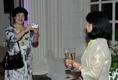 two women standing next to each other with wine glasses in their hands and one holding a cell phone