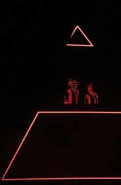 two people are sitting on top of a pyramid in the dark with red neon lights