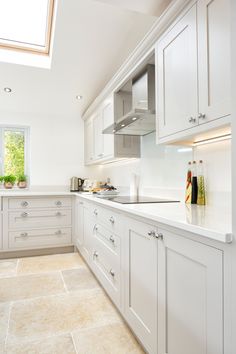 a kitchen with white cabinets and tile flooring in the center, along with a skylight