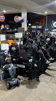 several men in black jackets and helmets are sitting on top of a car at a gas station