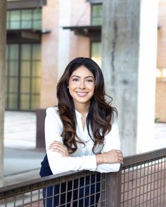 a woman leaning on a fence with her arms crossed and looking at the camera while smiling