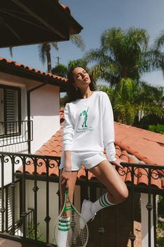 a woman posing with a tennis racquet in front of a house and palm trees