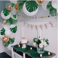 a table topped with cake and candles next to palm leaf decorations on the wall above it