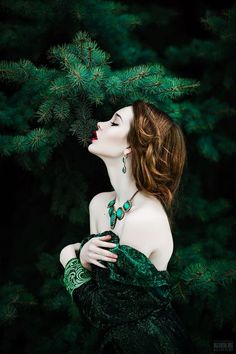 a woman with long hair and green dress is looking up into the sky while holding her hands on her chest