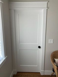 a white door in the corner of a room with a wicker chair next to it