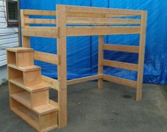 a wooden bunk bed sitting next to a blue tarp covered building with stairs leading up to it