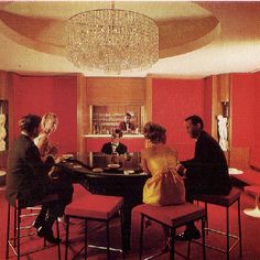 a group of people sitting around a table in a room with red walls and chandelier