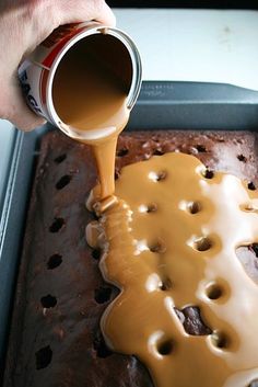 a person pouring caramel sauce on top of a chocolate cake in a baking pan