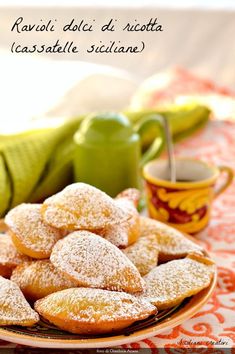 a plate full of powdered sugar cookies next to a cup of coffee and a green teapot