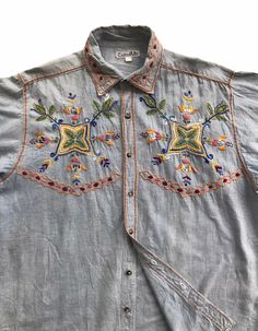 "Description: Here's an awesome vintage 70s chambray shirts in blue jeans, featuring hand embroidered bohemian patterns. This top is full of colorful florals embroidery. The fabric is soft and lightweight, so suitable for wearing in summer or spring days. It can be matched with jeans or shorts. It's a rare item, unique detailing, vintage casual style, lightweight and comfortable. Features: - Vintage chambray with floral embroidery. - Blue jeans. - Unique and rare detailing. - Hand embroidery work. Size:  - Length (centre of back neckline to bottom): 27 - 29\" - Armpit to armpit: 46\" - Shoulder to shoulder: 17.5\" - Sleeves (shoulder to cuff): 21.5\" Pants / Shirts sizes can vary between brands and regions. So, please have a look at actual measurements above before making the purchase deci Classic Casual Outfit, Chambray Shirts, Jeans Unique, Bohemian Shirt, Embroidery Blue, Baker Shirts, Colorful Florals, Bohemian Pattern, Embroidery Top