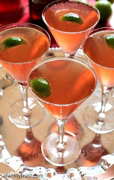 three martinis with lime garnish sit on a silver tray next to red wine glasses