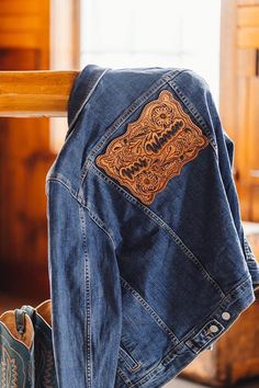 a denim jacket with an embroidered dragon on the back hanging from a rail in front of a window