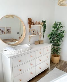 a baby's room with a dresser, mirror and potted plant in the corner