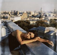 a woman leaning on the edge of a building with her arm resting on her chest