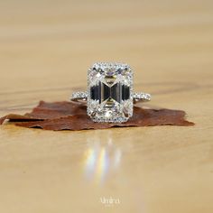 a fancy engagement ring with an emerald center surrounded by diamonds on top of a leaf