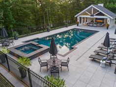 an outdoor swimming pool with lounge chairs and umbrellas next to it, surrounded by trees