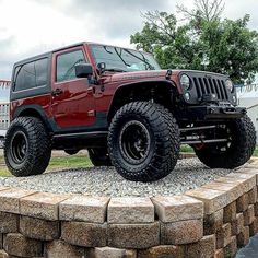 a red jeep parked on top of a pile of rocks in front of a building