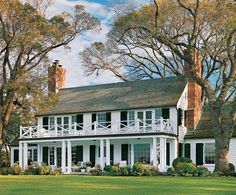 a large white house sitting on top of a lush green field next to tall trees