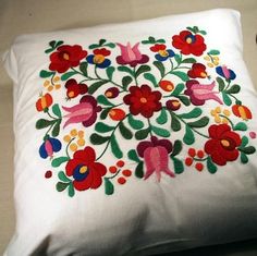 a white pillow with colorful flowers and birds embroidered on the front, sitting on a table