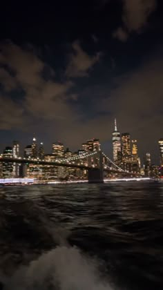 the city skyline is lit up at night as seen across the water from brooklyn bridge