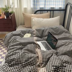 a laptop computer sitting on top of a black and white checkered comforter in a bedroom