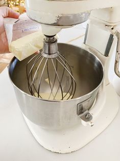 a hand is holding a whisk in a metal bowl on top of a mixer