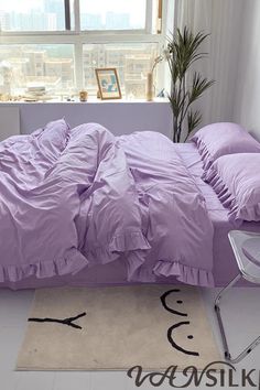 a bed with purple sheets and pillows in a room next to a large window overlooking the city