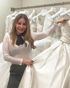 a woman standing in front of dresses on display at a bridal shop with her hands on the skirt