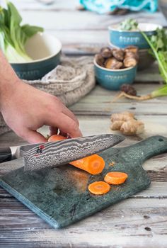 a person is cutting carrots with a knife on a wooden table next to other vegetables