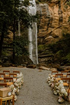 an outdoor ceremony setup with chairs and flowers in front of a waterfall