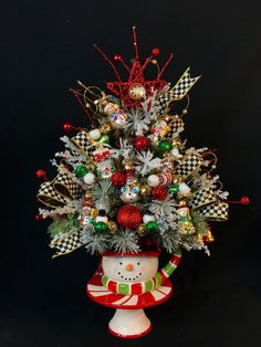 a decorated christmas tree in a red and white pot on a black background with ornaments