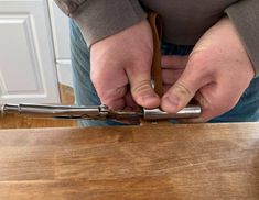 a person is holding a pair of scissors in their right hand while standing on a wooden table