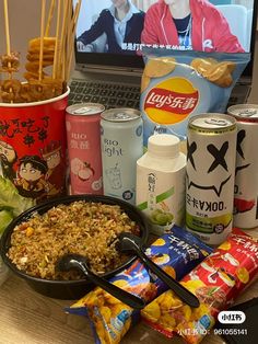 an open laptop computer sitting on top of a wooden table next to snacks and drinks