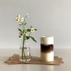 there is a vase with flowers in it next to a small glass cup on the table