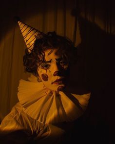 a creepy clown with his face painted yellow and wearing a white hat, standing in front of a curtain