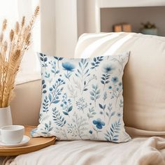 a coffee cup on a tray next to a pillow with blue flowers and leaves in it