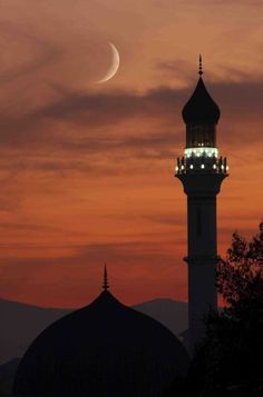 the moon is setting behind a tall building