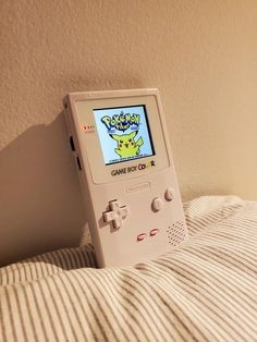 an old nintendo gameboy sitting on top of a bed next to a striped pillow