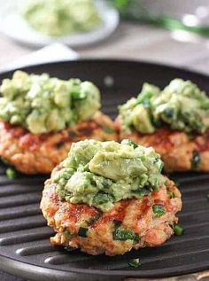 three crab cakes with guacamole on top are sitting on a grill pan