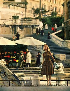 a woman standing in front of some steps with umbrellas on it and people walking around