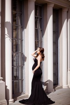 a woman in a black dress is standing on the sidewalk near some columns and windows