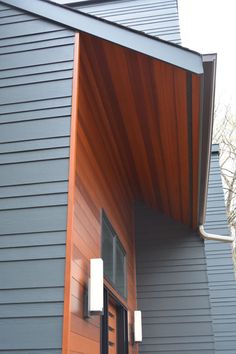 the side of a gray house with wood trimming and an awning over it