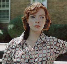 a woman with red hair and blue eyes wearing a patterned shirt looking at the camera