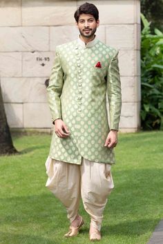 a man in a green and white sherwanit suit standing on the grass