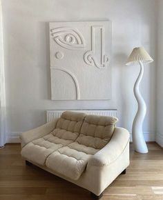 a living room with a couch, lamp and art work on the wall behind it