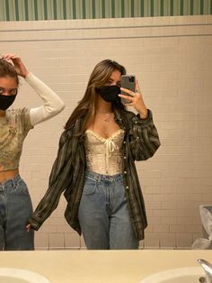 two women wearing face masks while standing in front of a mirror