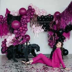 a woman sitting on the floor in front of some balloons and black horses with pink fringes