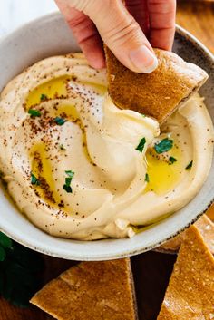 a person dipping hummus into a bowl with pita bread on the side and garnished with parsley