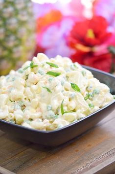 a bowl filled with macaroni salad on top of a wooden table next to flowers